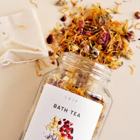 2: A mix of dried botanicals and a small muslin pouch spill out of a glass jar with a white label.