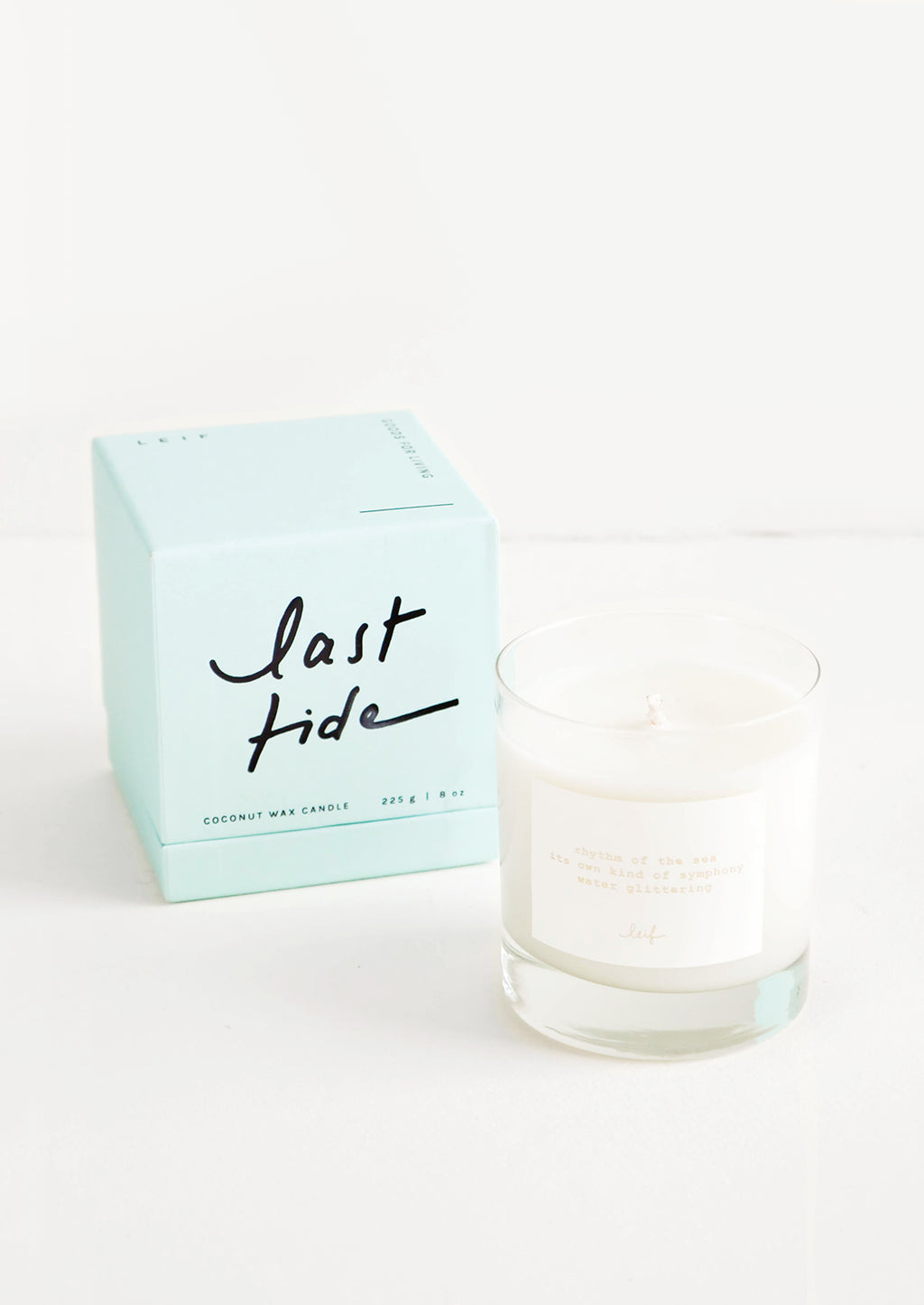 Last Tide: A glass candle with a white label sits next to a pale blue colored box reading "last tide" in black cursive text.