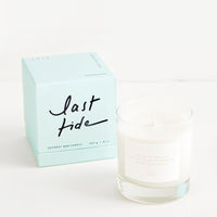 Last Tide: A glass candle with a white label sits next to a pale blue colored box reading "last tide" in black cursive text.A glass candle with a white label sits next to a peach colored box reading "lost A glass candle with a white label sits next to a peach colored box reading "lost letters" in black cursive text.letters" in black cursive text.