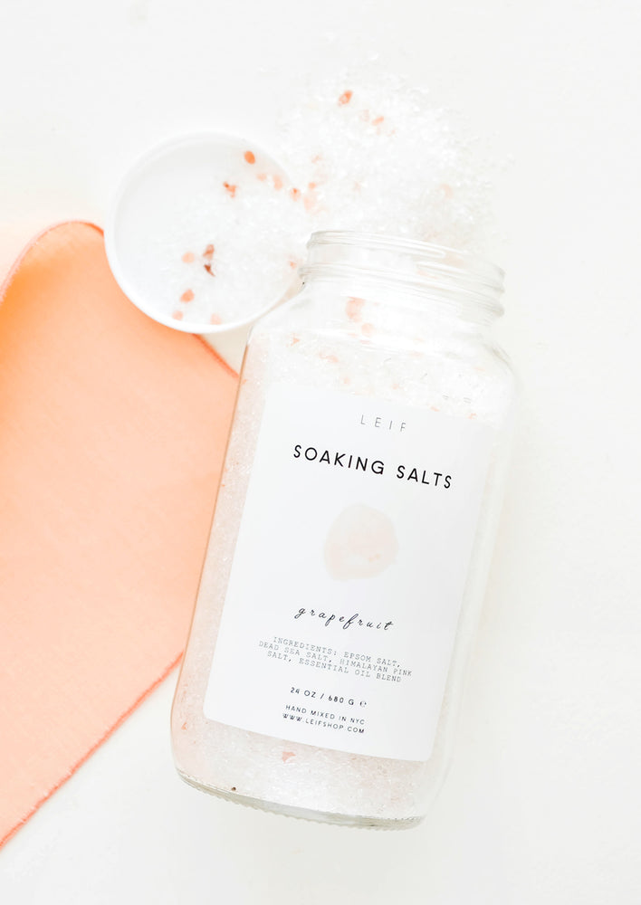 Grapefruit: An unlidded tall glass jar with a simple white and pink label and white salt crystals spilling out of it.