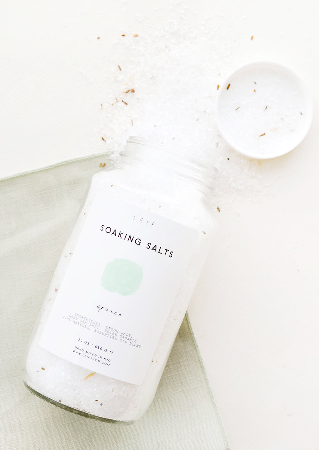 Spruce: An unlidded tall glass jar with a simple white and green label and white salt crystals spilling out of it.