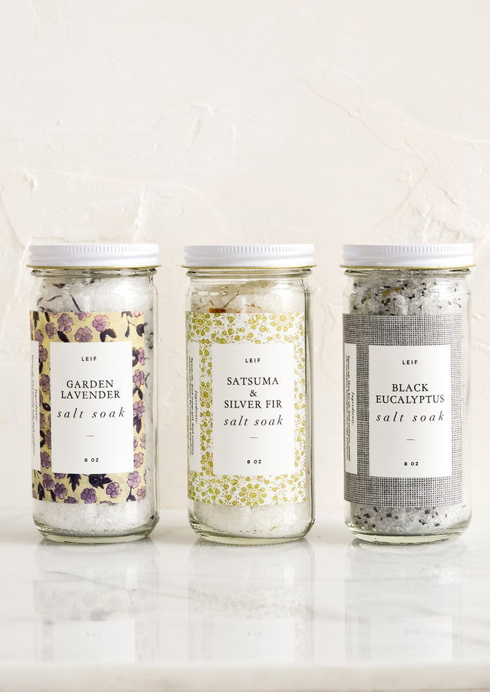 Three glass jars with decorative labels containing bath salt soaks.