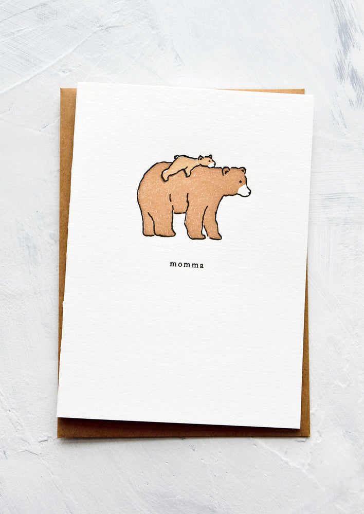 A letterpress printed greeting card with an image of a baby bear laying on back of larger bear. Text underneath reads "momma".