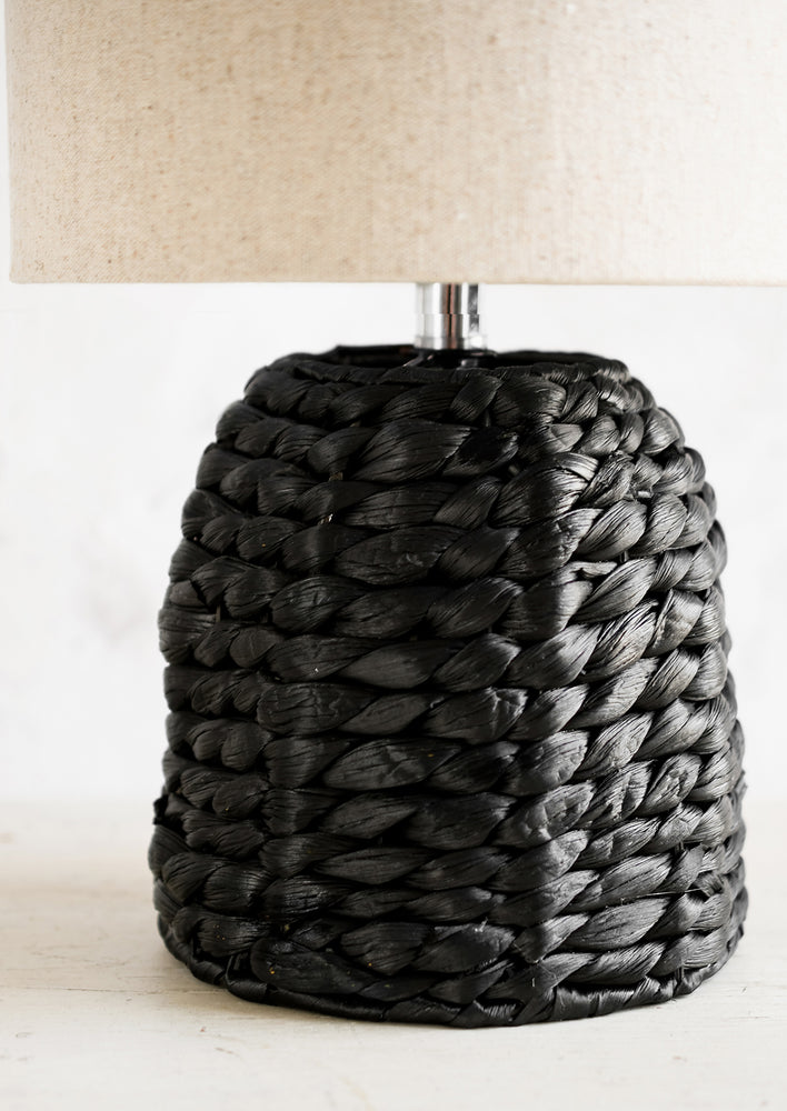 A table lamp with black woven base and linen shade.