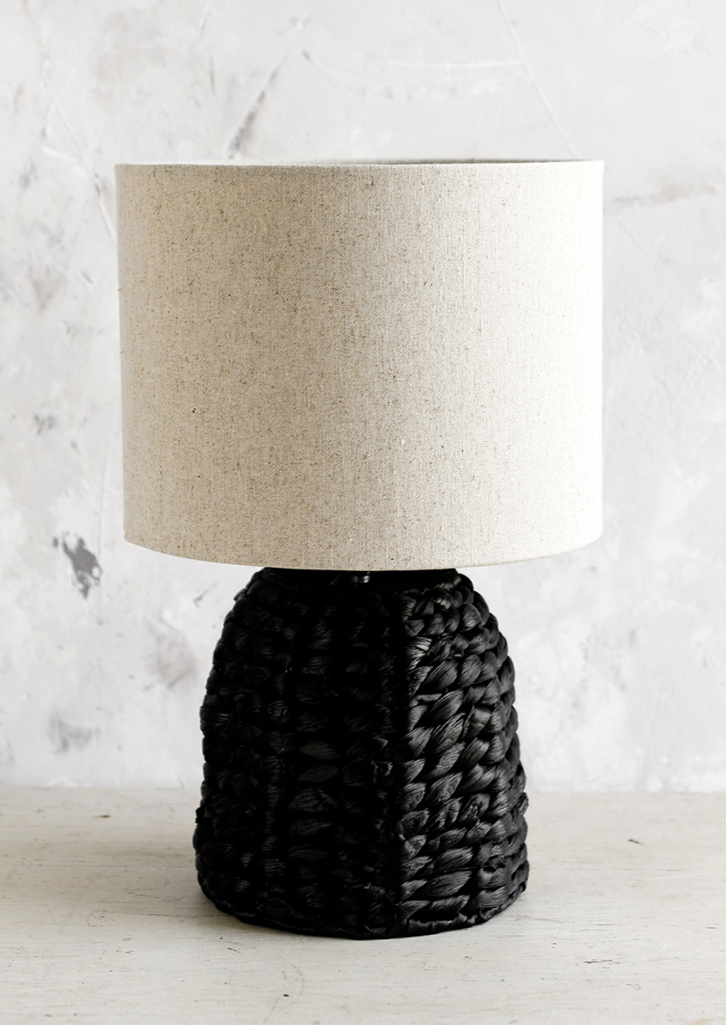 1: A table lamp with black woven base and linen shade.
