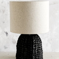 1: A table lamp with black woven base and linen shade.