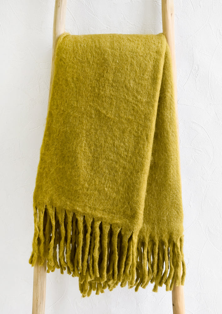 2: A chartreuse mohair blanket with long tassel fringe displayed on a ladder.