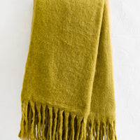 2: A chartreuse mohair blanket with long tassel fringe displayed on a ladder.