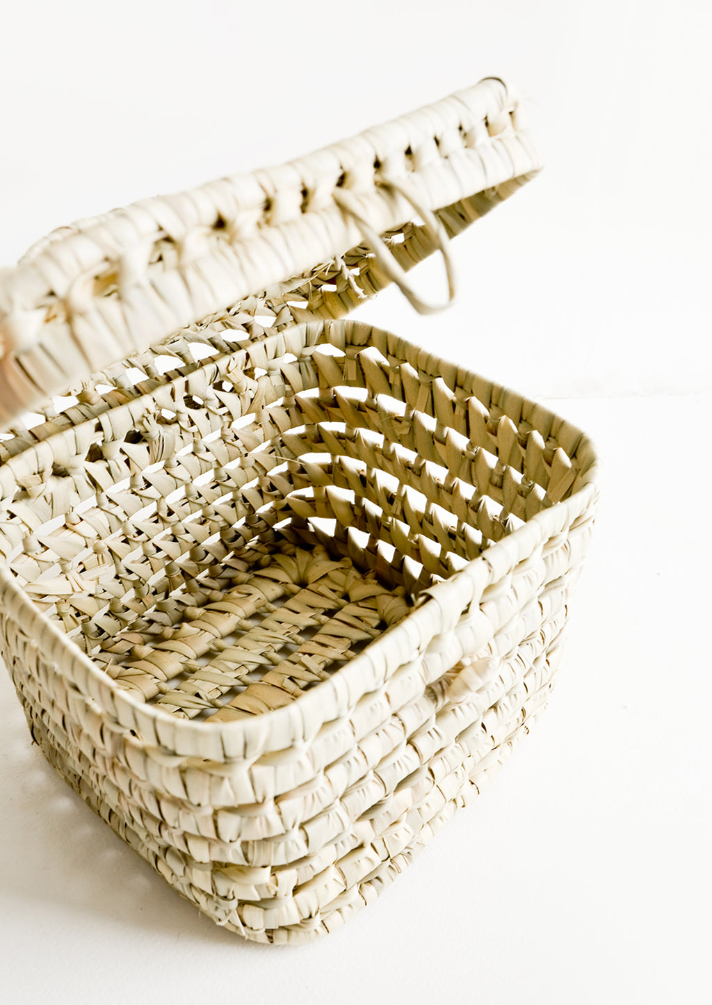2: The empty interior of a square, lidded basket woven from natural palm leaf.