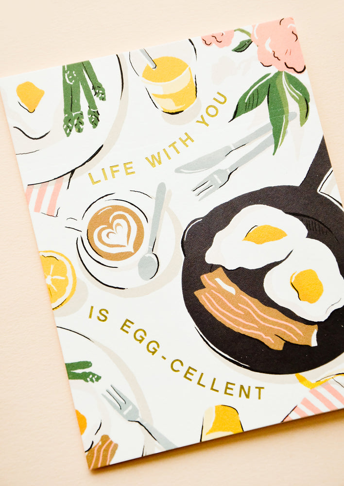1: Greeting card with breakfast scene and gold letters reading "Life with you is egg-cellent"