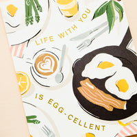 1: Greeting card with breakfast scene and gold letters reading "Life with you is egg-cellent"