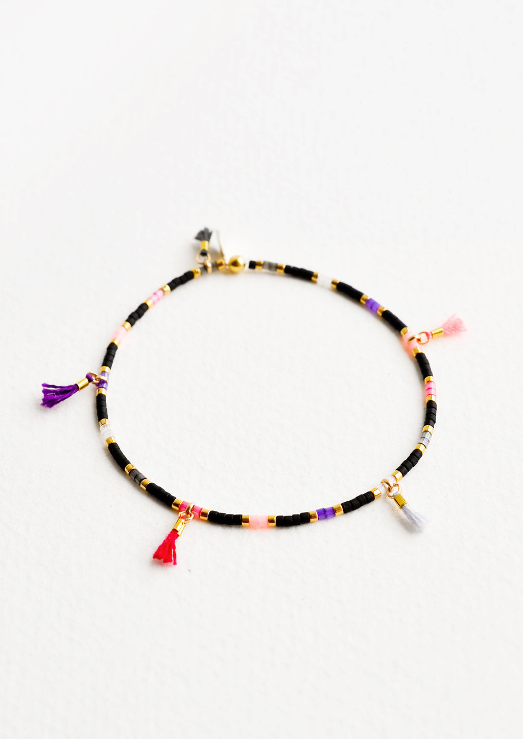 Black Multi: Bracelet featuring black, gold, pink and purple glass beads interspersed with 5 small multicolor string tassels on an elastic cord.
