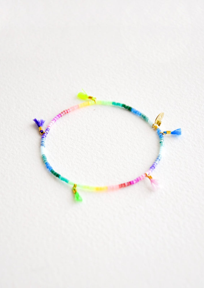 Bracelet featuring multicolor neon rainbow glass beads interspersed with 5 small multicolor string tassels on an elastic cord.