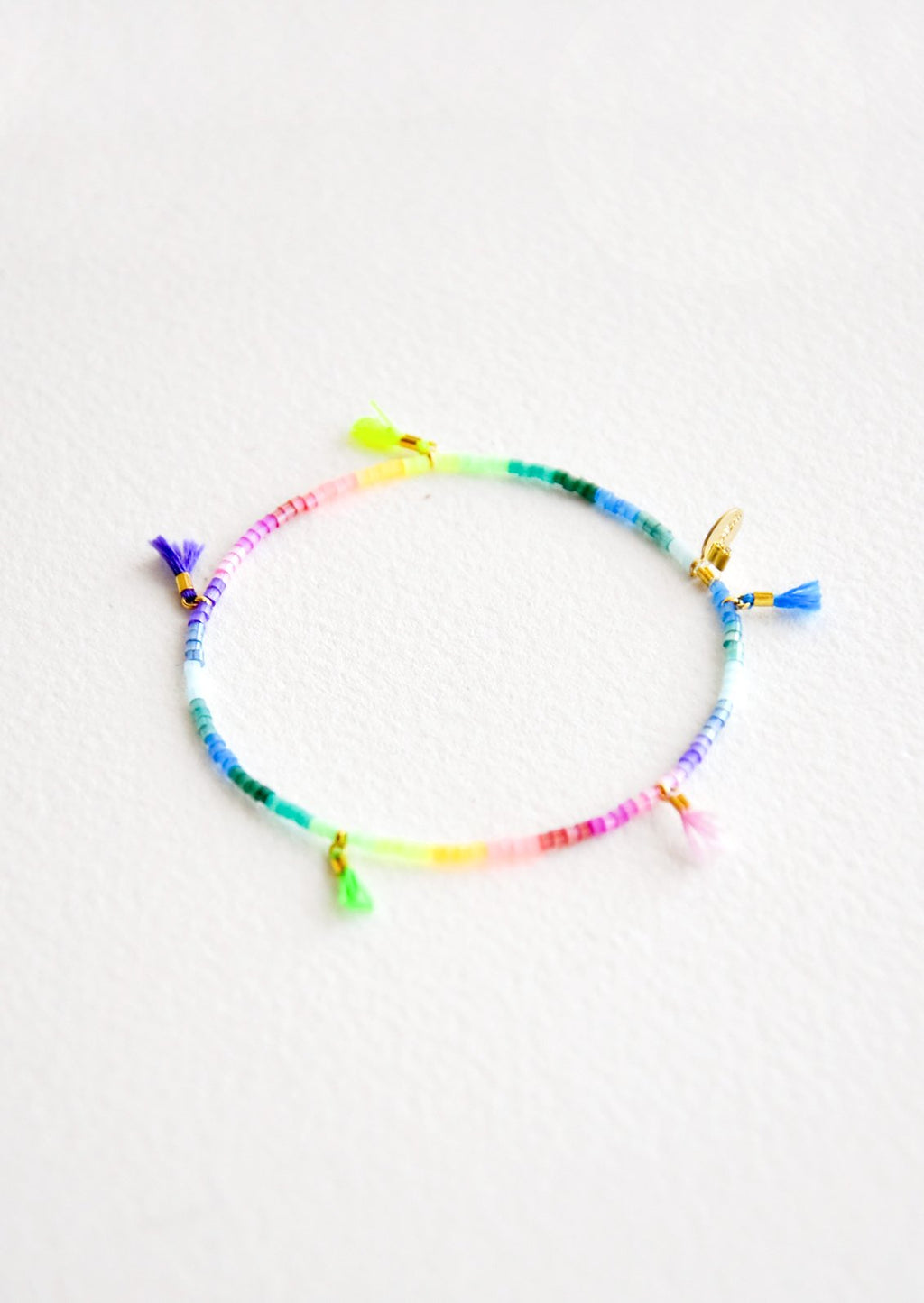 Rainbow Gradient: Bracelet featuring multicolor neon rainbow glass beads interspersed with 5 small multicolor string tassels on an elastic cord.