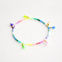 Rainbow Gradient: Bracelet featuring multicolor neon rainbow glass beads interspersed with 5 small multicolor string tassels on an elastic cord.