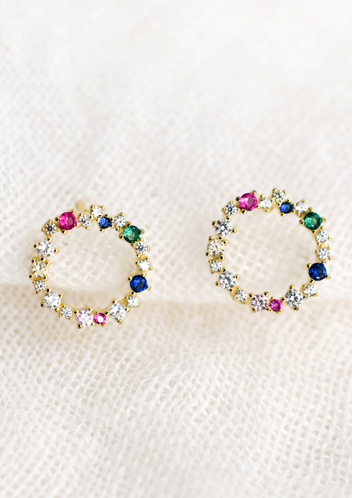 A pair of gold circle shaped studs with mix of clear and colored crystals.