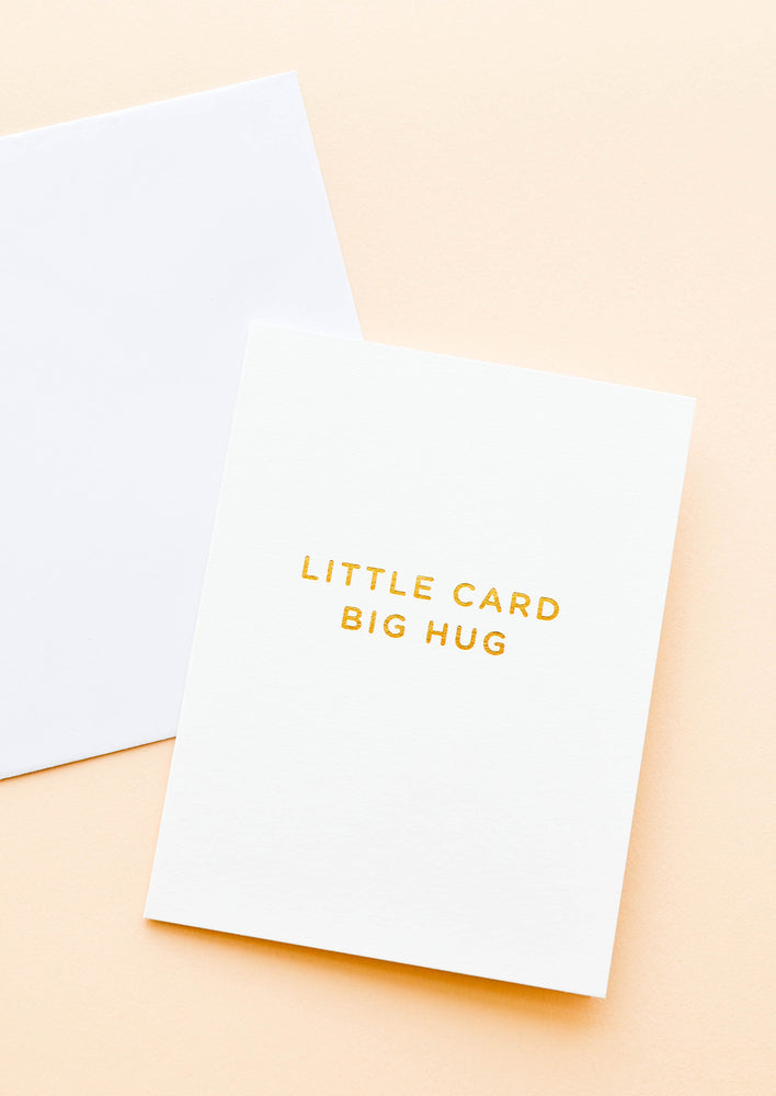 A white greeting card with the words "little card big hug" in gold foil.