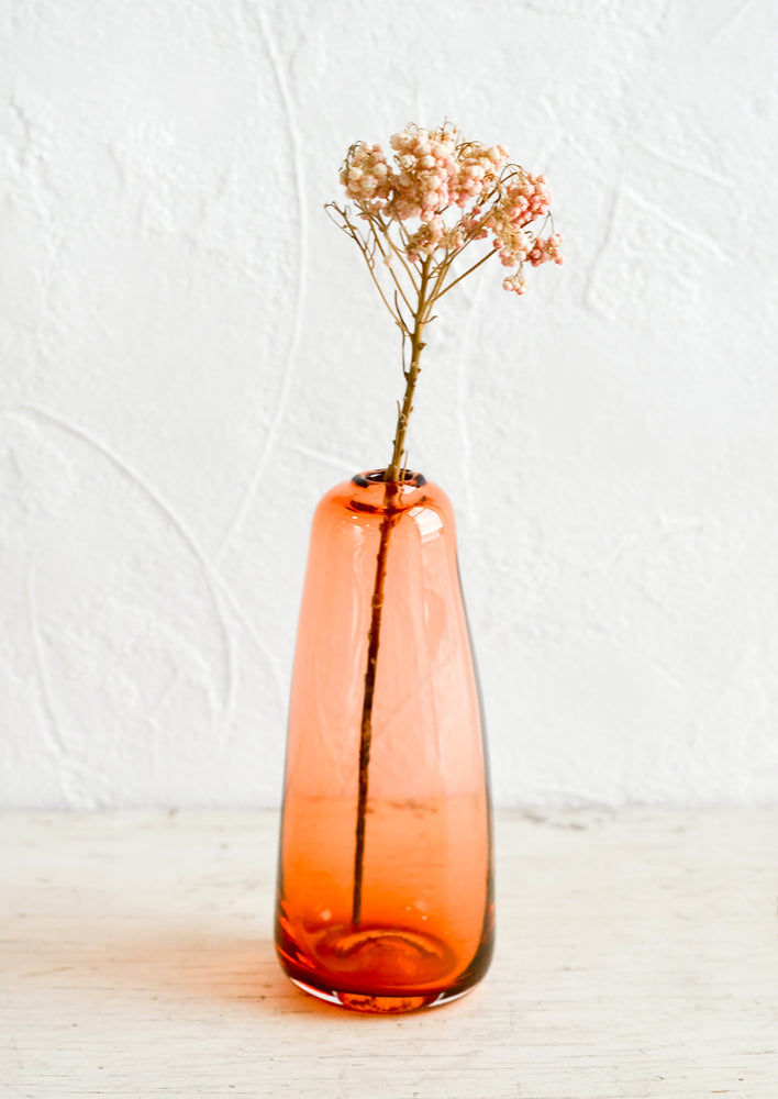 A tall glass bud vase in translucent red-orange.