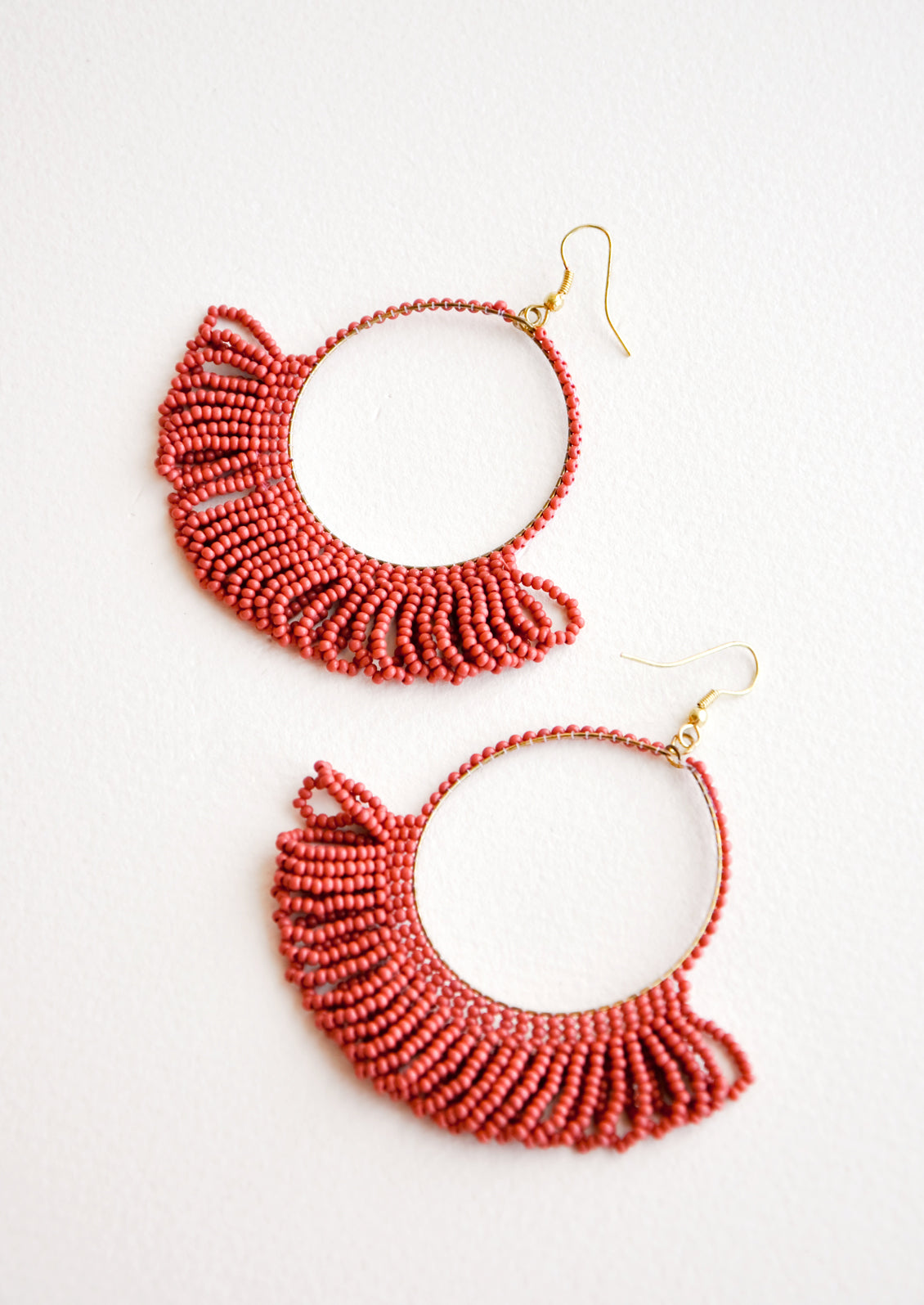 Dangling hoop earrings featuring dark red beads and accented with hanging beaded, looped fringe.