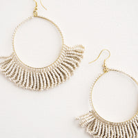 Vanilla: Dangling hoop earrings featuring light grey beads and accented with hanging beaded, looped fringe.