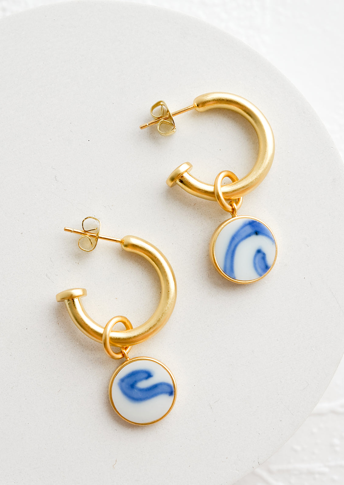 A pair of gold hoop earrings with blue and white pottery disc.