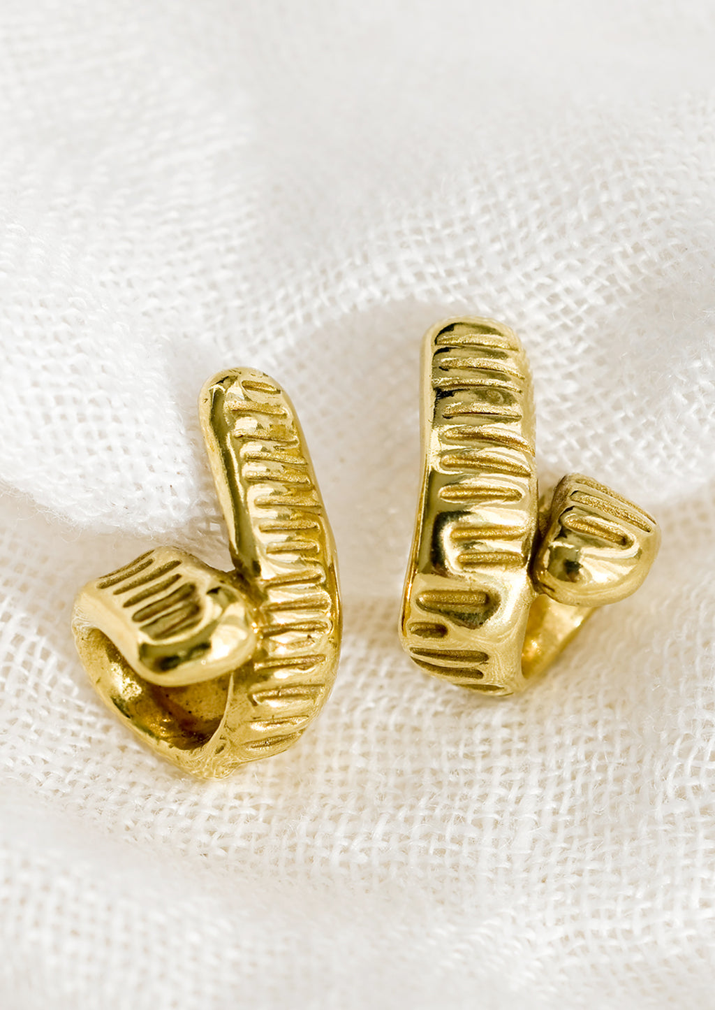 1: A pair of brass earrings with curled shape and line etched texture.