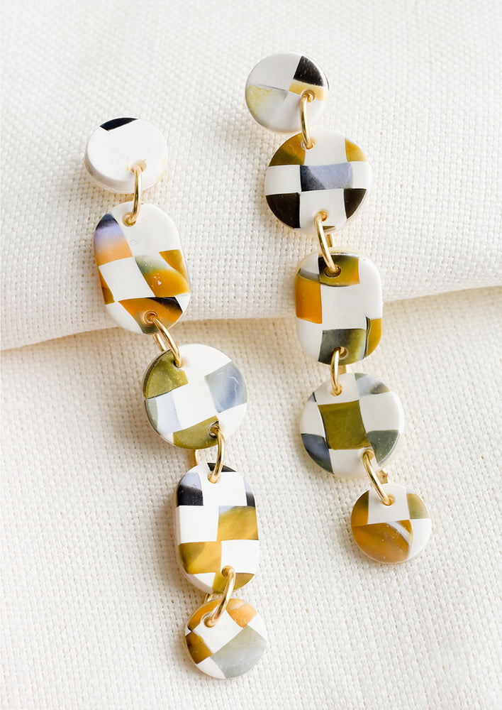 A pair of white clay drop earrings with multiple circle and oval shapes with multicolor checkered pattern.