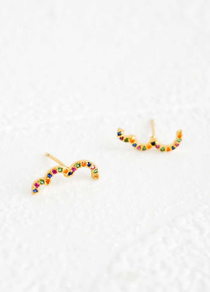 A pair of gold stud earrings in squiggly, half cloud-like shape with multicolor crystal detailing.