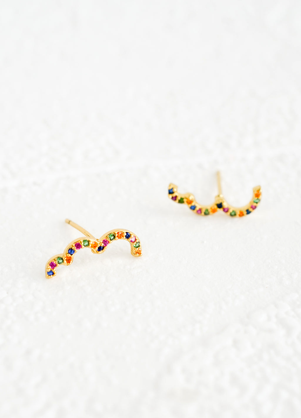 1: A pair of gold stud earrings in squiggly, half cloud-like shape with multicolor crystal detailing.