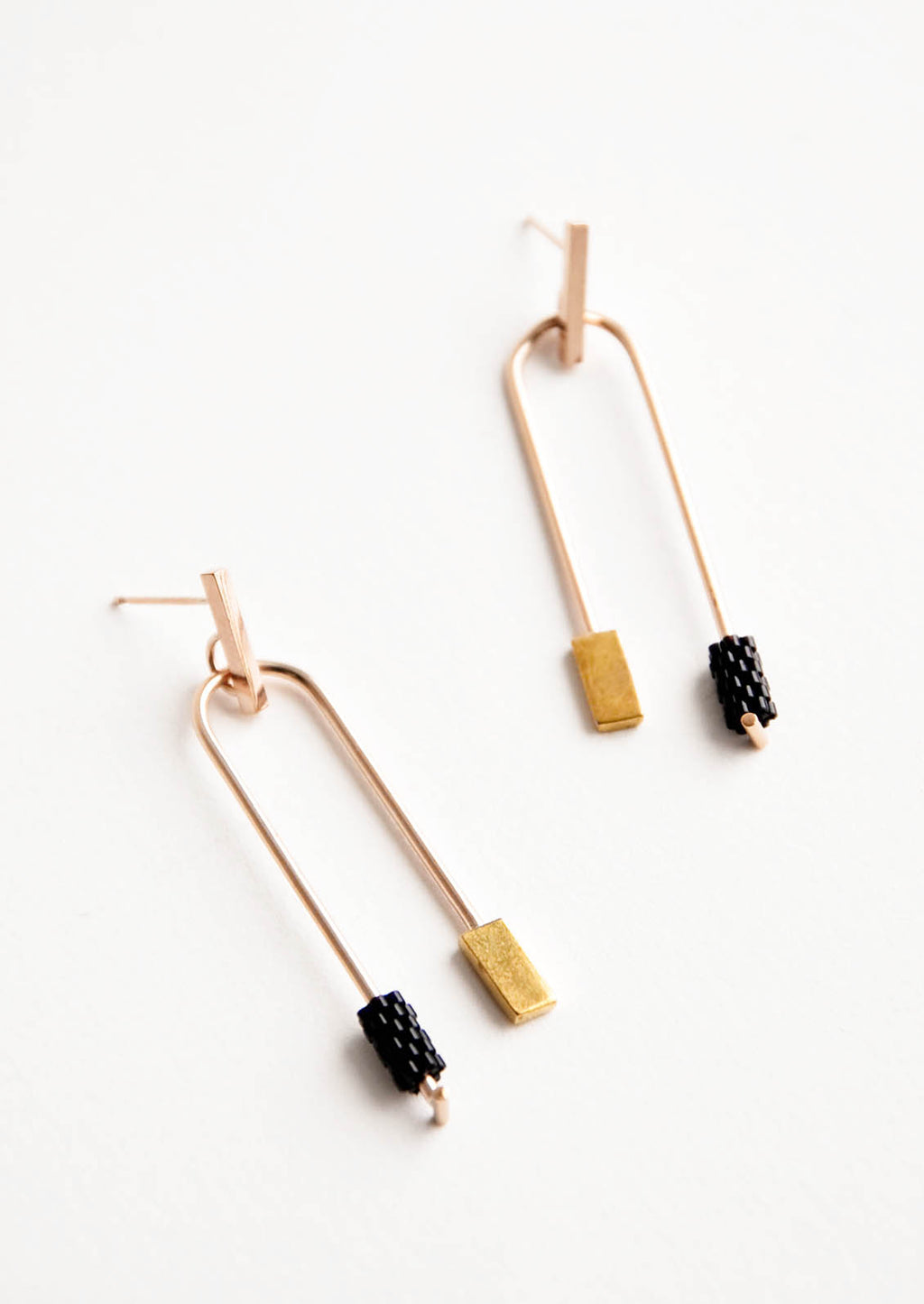 Onyx: Post back gold earrings with curved arc featuring one black beaded end and one square gold end.