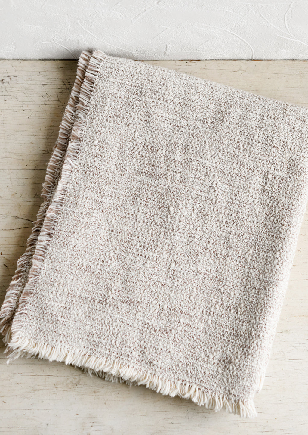 3: A textured boucle blanket with fringe trim in tan/white.