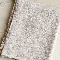 3: A textured boucle blanket with fringe trim in tan/white.