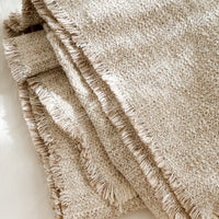 Birch Multi: A textured boucle blanket with fringe trim in tan/white.