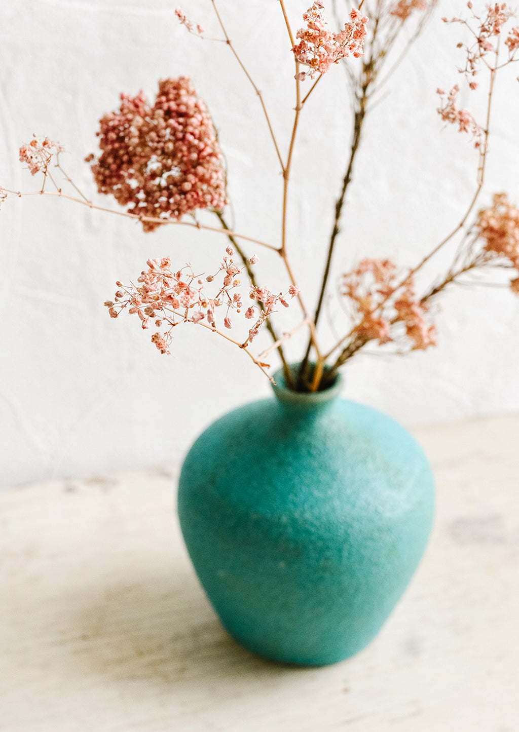 2: A textured turquoise ceramic vase with dried pink flowers inside.