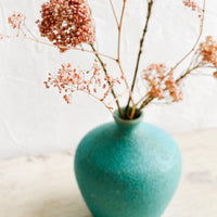 2: A textured turquoise ceramic vase with dried pink flowers inside.