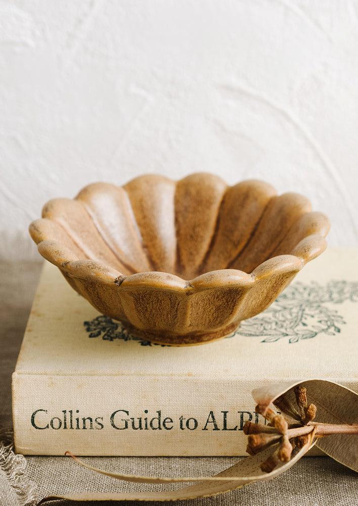 A brown flower shaped bowl styled on top a book.