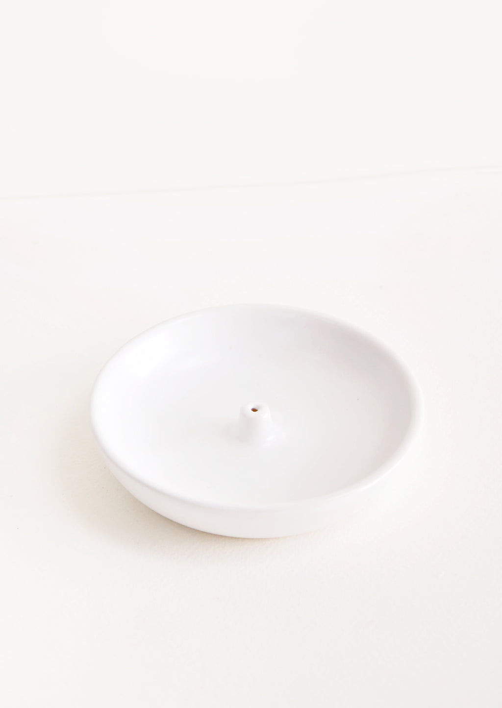 2: A simple white dish with a small hold at the center for holding incense.