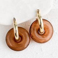 Coffee: A pair of brown resin donut shaped charms on gold hoop earrings.