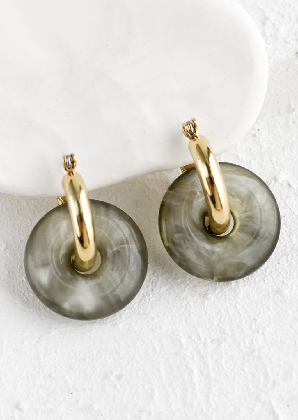 Pebble: A pair of grey resin donut shaped charms on gold hoop earrings.