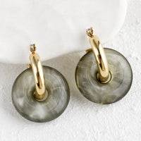 Pebble: A pair of grey resin donut shaped charms on gold hoop earrings.