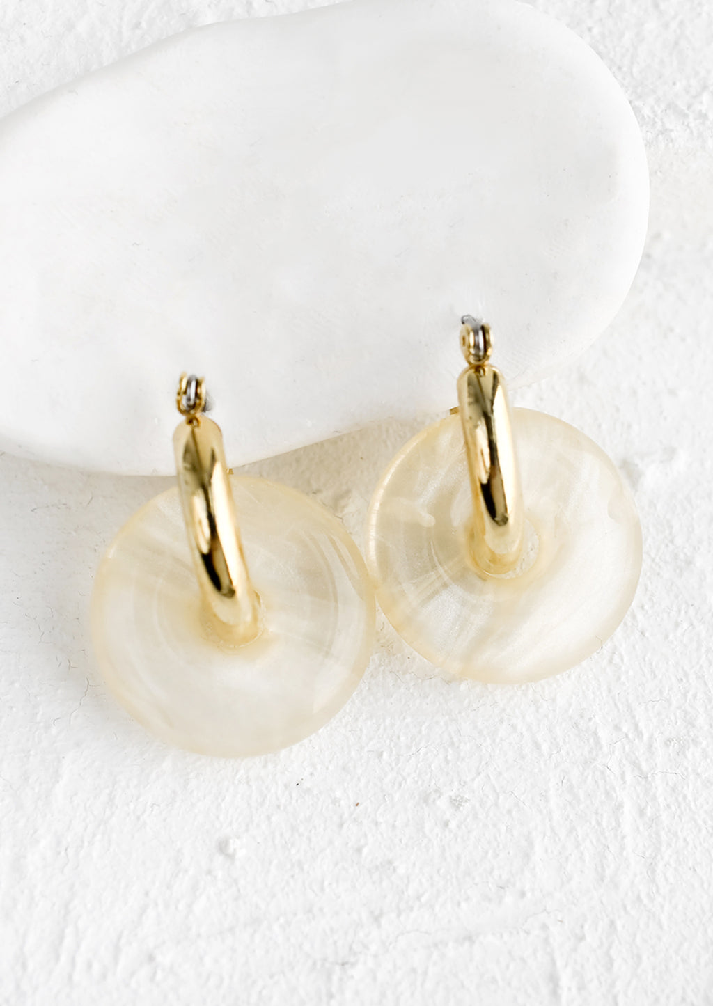Sugar: A pair of clear resin donut shaped charms on gold hoop earrings.