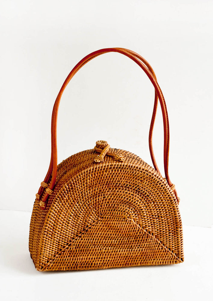 Half-oval shaped, structured handbag made from smoked rattan. Tanned leather carrying handles.