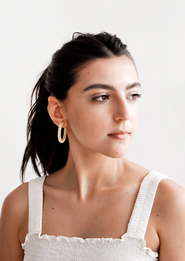 Model shot of woman wearing earrings and a white top.