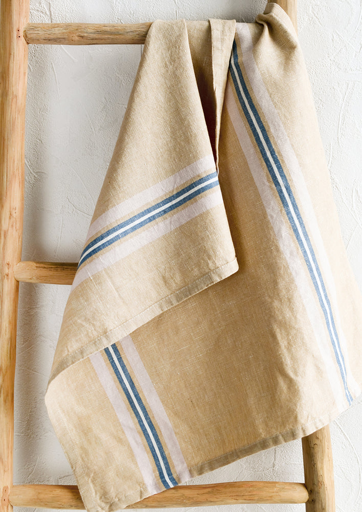 A tan tea towel with blue, pink and white vertical stripe.
