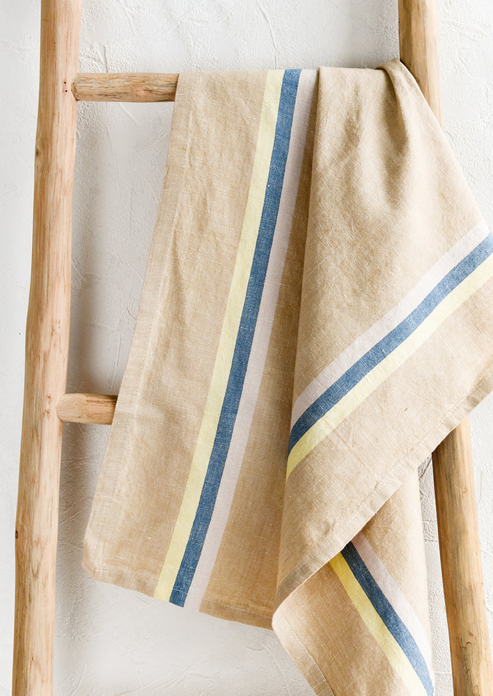 A tan tea towel with blue, pink and yellow vertical stripe.