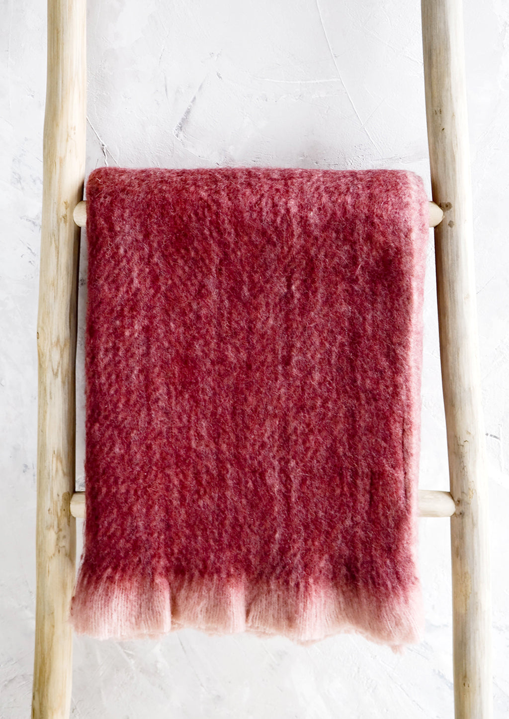 1: Plush, fuzzy blanket in wine red color with pale pink trim, displayed on ladder