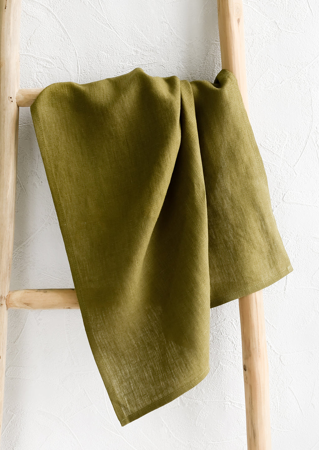Olive: A olive green linen tea towel draped on a wooden ladder.