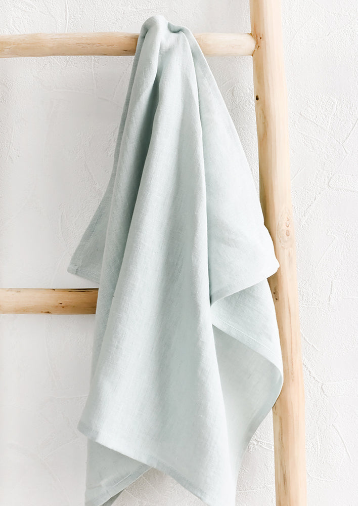 A seafoam linen tea towel draped on a wooden ladder.