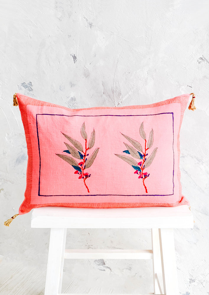 Decorative throw pillow in vibrant pink linen with block printed floral detail and jute tassels at corners