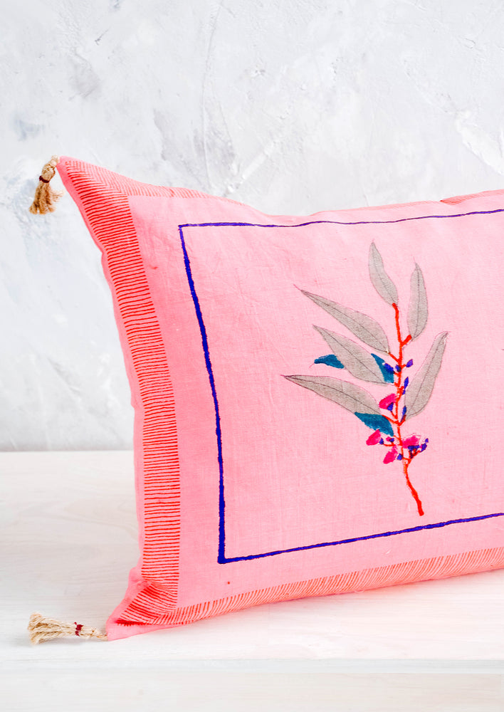 Decorative throw pillow in vibrant pink linen with block printed floral detail and jute tassels at corners